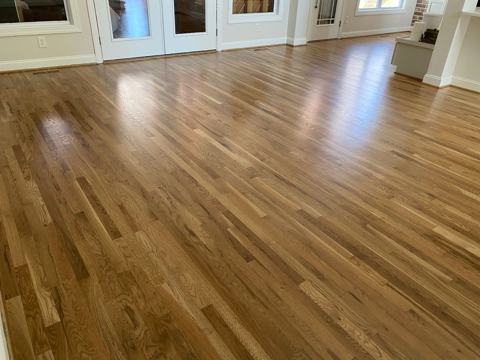 Refinished hardwood floor in a natural tone, French doors along the back wall